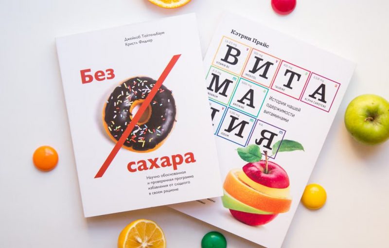 Top view of fresh oranges and apple placed near books about healthy lifestyle on white background